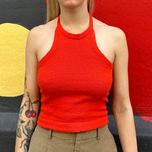 May include: A bright orange halter top made of a soft, textured fabric. The top has a simple, classic design and is cropped at the waist.