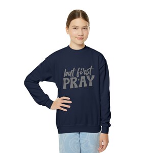 Puede incluir: Una sudadera azul marino con el texto "but first PRAY" en letras grises.