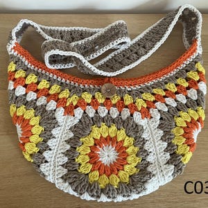 Peut inclure: Sac à bandoulière crocheté à motif granny square. Il présente un mélange de couleurs marron, blanc, orange et jaune. Il est orné d'un bouton en bois et d'une bandoulière assortie. Le sac porte l'inscription "C03".