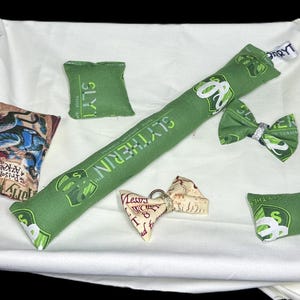 Peut inclure: Un ensemble de jouets pour chat en tissu vert et blanc sur le th&egrave;me des maisons de Poudlard. Les jouets comprennent un jouet long et rectangulaire avec les mots "Serpentard" imprim&eacute;s dessus, un petit jouet carr&eacute; avec le mot "Serpentard" imprim&eacute; dessus, un petit jouet carr&eacute; avec les mots "Gryffondor" imprim&eacute;s dessus, un petit jouet carr&eacute; avec les mots "Poufsouffle" imprim&eacute;s dessus, et un petit jouet carr&eacute; avec les mots "Serdaigle" imprim&eacute;s dessus. Il y a aussi un petit n&oelig;ud papillon avec les mots "Serpentard" imprim&eacute;s dessus.