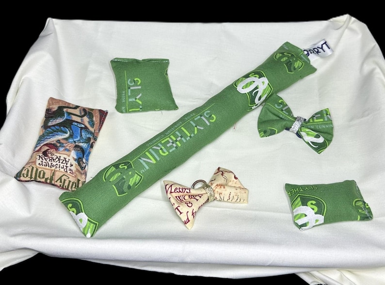 Peut inclure: Un ensemble de jouets pour chat en tissu vert et blanc sur le th&egrave;me des maisons de Poudlard. Les jouets comprennent un jouet long et rectangulaire avec les mots "Serpentard" imprim&eacute;s dessus, un petit jouet carr&eacute; avec le mot "Serpentard" imprim&eacute; dessus, un petit jouet carr&eacute; avec les mots "Gryffondor" imprim&eacute;s dessus, un petit jouet carr&eacute; avec les mots "Poufsouffle" imprim&eacute;s dessus, et un petit jouet carr&eacute; avec les mots "Serdaigle" imprim&eacute;s dessus. Il y a aussi un petit n&oelig;ud papillon avec les mots "Serpentard" imprim&eacute;s dessus.