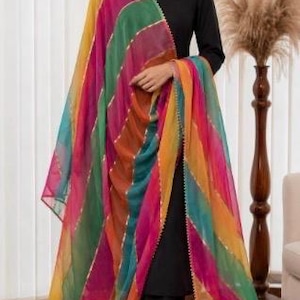 May include: A black long-sleeved top and matching black trousers paired with a vibrant, multi-coloured striped dupatta. The sheer fabric features diagonal bands of yellow, green, orange, and pink, accented with thin, metallic gold-toned trim.