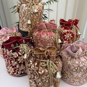 May include: A selection of velvet drawstring bags in shades of red, pink, and brown. Each bag features detailed gold embroidery and sparkling gemstones. The bags are finished with gold drawstrings and tassels.