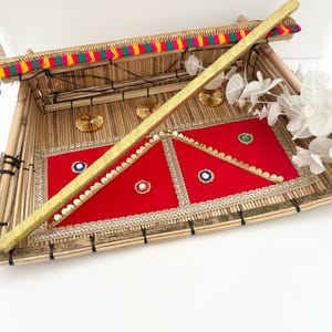 May include: A bamboo tray with a red velvet lining and gold accents. The tray is decorated with a gold stick and white flowers.