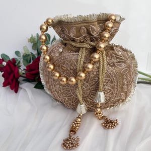 Peut inclure: Un sac à cordon brodé marron avec des perles et des glands dorés. Le sac présente des motifs floraux complexes et une poignée perlée. Le fond comprend une rose rouge et du tissu blanc.