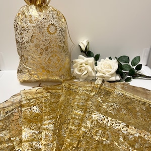 Può includere: Un set di sacchetti di organza trasparente dorati con un motivo floreale. I sacchetti sono piegati e impilati uno sopra l'altro. Sullo sfondo ci sono rose bianche.