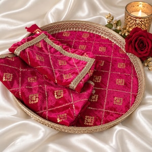 May include: A round gold-toned metal tray featuring a fuchsia velvet fabric inlay with a gold sequin grid pattern and a matching fuchsia velvet pouch with gold lace trim, accompanied by a single red rose and a gold candle holder with a lit candle.