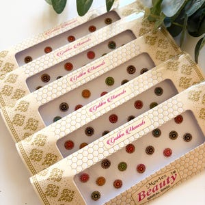 Op de afbeelding: Er worden verschillende dozen Mories Beauty Bridal Bindi getoond. Elke doos bevat meerdere kleurrijke, cirkelvormige bindis met ingewikkelde ontwerpen. De dozen zijn crèmekleurig met gouden patronen en de tekst "Golden Moments" is zichtbaar.