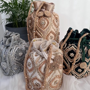 May include: Four ornate drawstring bags in silver, gold, cream, and emerald green. Each bag is embellished with intricate beadwork and sparkling accents. The bags have beaded handles and are made of velvet.