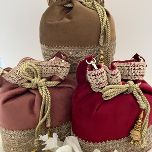 Peut inclure: Trois sacs en velours à cordon de serrage, de couleurs marron, mauve et rouge. Chaque sac est orné d'une bordure en dentelle décorative à la base et autour de l'ouverture à cordon. Des cordes et des glands dorés ajoutent une touche élégante.