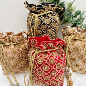 Può includere: Una collezione di borse decorative con coulisse in vari colori. Le borse sono impreziosite da perline e ricami color oro. I colori includono nero, rosso e oro. Le borse hanno una consistenza simile al velluto.