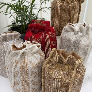 Puede incluir: Una colección de bolsos con cordón y cuentas en varios colores, incluyendo dorado, plateado y rojo. Los bolsos presentan patrones intrincados y están adornados con cuentas y lentejuelas. Los bolsos se exhiben sobre una superficie blanca.