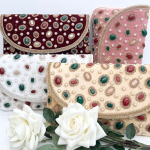 May include: Four different velvet clutches with jeweled embellishments. The clutches are in shades of pink, white, cream, and burgundy. Each clutch has a different pattern of jewels, including pearls, rhinestones, and coloured stones.