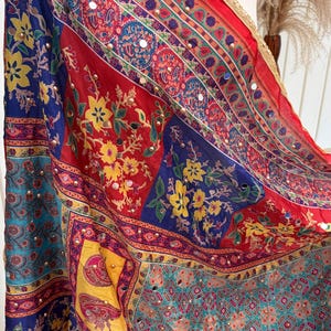 Könnte beinhalten: Ein farbenfrohes Tuch mit Patchwork-Design. Es zeigt eine Mischung aus Rot, Blau, Gelb und Türkis, verziert mit Blumenmustern, Paisley-Motiven und kleinen, reflektierenden Verzierungen. Die Kanten sind mit Gold verziert.