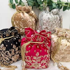 May include: A selection of velvet drawstring bags in shades of gold, silver, black, fuchsia, and cream. Each bag features detailed gold embroidery and sequin embellishments. The bags have gold rope drawstrings and tassels.