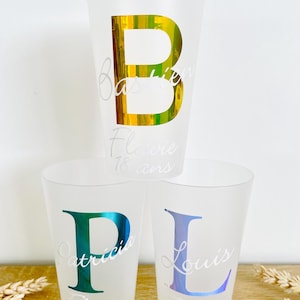 Può includere: Tre bicchieri di plastica opaca con nomi personalizzati e il testo "18 ans" stampato su di essi. I bicchieri presentano le lettere B, P e L in oro iridescente, turchese e viola.