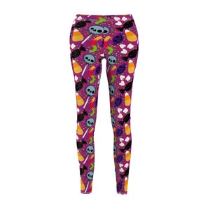 Puede incluir: Leggings morados con un patrón repetido de caramelos, calaveras y confeti con temática de Halloween. Los leggings presentan caramelos de maíz, piruletas y caramelos envueltos. El diseño está sobre un fondo morado liso.