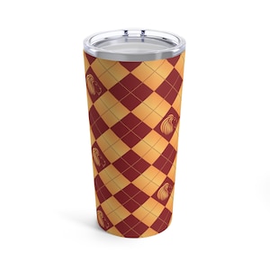Puede incluir: Un vaso de acero inoxidable con un patrón de rombos rojo y dorado y un diseño de cabeza de león.
