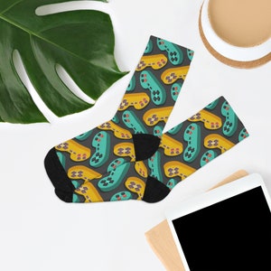 May include: A pair of black socks with a colorful pattern of video game controllers. The controllers are in shades of yellow, green, and blue.