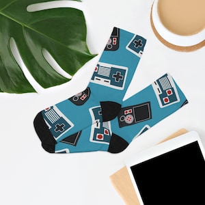 May include: A pair of blue socks with a pattern of retro video game controllers. The socks are black at the toes and heels.