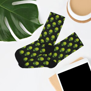 May include: A pair of black socks with a green alien face pattern. The socks are folded and laid out on a white surface.