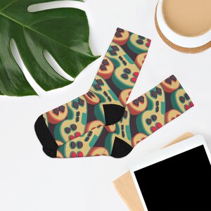 Puede incluir: Un par de calcetines con un patrón colorido de mandos de videojuegos retro. Los calcetines son amarillos, verdes, rojos y negros.