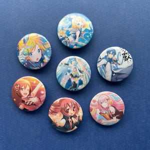 Puede incluir: Siete botones redondos con ilustraciones de personajes de estilo anime. Los botones presentan diseños coloridos con varios personajes en diferentes poses y atuendos. El fondo es azul oscuro.