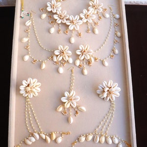 May include: A set of white shell jewelry, including a necklace, earrings, and a hairpiece. The jewelry is made with white seashells and gold accents.
