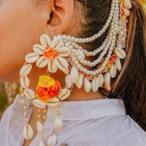 May include: A large, white shell earring with orange and yellow flowers and pearl accents. The earring is attached to a chain of white pearls.