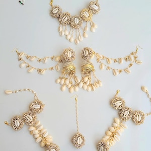 May include: A set of white shell jewellery, including a necklace, earrings, a maang tikka, and a bracelet. The jewellery is made with white shells and gold accents.