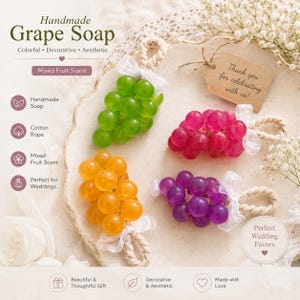 Può includere: Saponi fatti a mano a forma di grappolo d'uva in verde, rosa, arancione e viola, legati con nastro bianco e corda di cotone. I saponi sono etichettati "Handmade Grape Soap" e "Mixed Fruit Scent". Un'etichetta recita "Thank you for celebrating with us!"