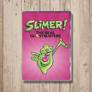 May include: A DVD case featuring the animated series "Slimer! and The Real Ghostbusters." The cover has a pink background with a green slime monster character and the show's title in green lettering. The Ghostbusters logo is also visible.
