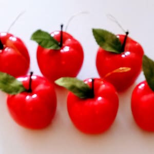May include: Six red artificial apples with green leaves, perfect for decorating a fall or autumn themed event.