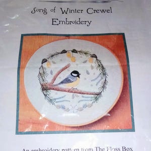 May include: An embroidery pattern from The Floss Box, featuring a detailed crewel embroidery design. The design showcases a bird perched on a branch, surrounded by a winter wreath. The text "Song of Winter Crewel Embroidery" is visible.