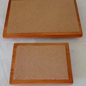 May include: Two rectangular wooden serving trays. The trays have a light brown cork surface set within a darker brown wooden frame. One tray is larger than the other. The trays are likely used for serving food or drinks.