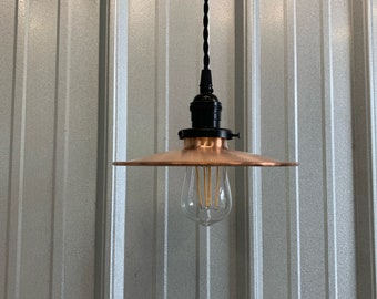 May include: A copper pendant light with a black cord and a black socket. The light is hanging from a metal ceiling. The light has a simple design and is perfect for a modern or industrial style home.