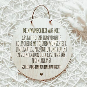 May include: A round wooden sign with a light brown finish and a brown leather hanging loop. The sign features engraved text in a dark brown color, including a heart symbol. The background is a textured white surface.