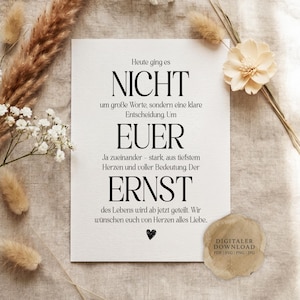 May include: A white rectangular card featuring black printed German text that reads: Heute ging es NICHT um große Worte, sondern eine klare Entscheidung. Um EUER Ja zueinander - stark, aus tiefstem Herzen und voller Bedeutung. Der ERNST des Lebens wird ab jetzt geteilt. Wir wünschen euch von Herzen alles Liebe. A small black heart icon is printed at the bottom.