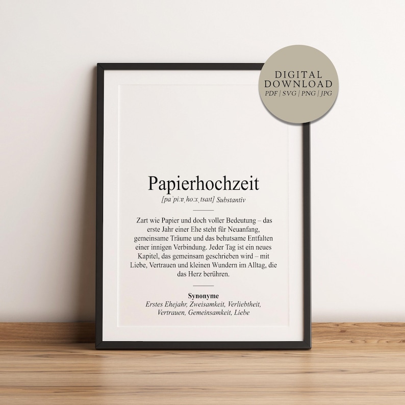 May include: A framed print with the German word "Papierhochzeit" in a black frame. The print includes text describing the meaning of the word, synonyms, and a "DIGITAL DOWNLOAD" label. The print is on a wooden surface.