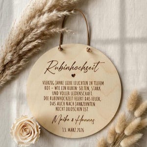 Könnte beinhalten: Runder Holzschild mit dem Text "Rubinhochzeit" und weiterem deutschen Text, einschließlich Namen und Datum. Das Schild hat eine Lederschlaufe zum Aufhängen und ist von Trockenblumen und einer Rose umgeben.