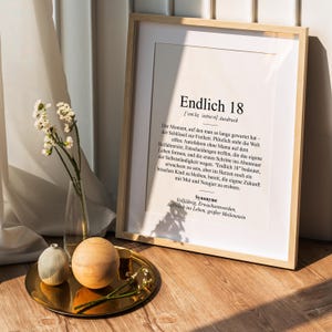 May include: A framed print with a white background and black text. The text reads "Endlich 18" and defines the word as a German expression for "turning 18". The text also includes synonyms for the word, such as "coming of age" and "adult".