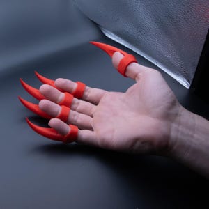 May include: A set of five red claw-like finger covers. The covers are made of a flexible material and are designed to fit over the fingertips.