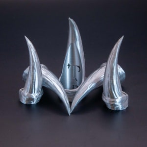 May include: Four silver-coloured, 3D printed, claw-like rings. The centre ring has the letter "T" engraved on it.