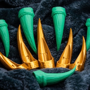 May include: A set of eight claws, four are green and four are gold. The claws are arranged in a semi-circle on a dark grey fuzzy surface.