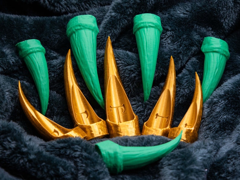 May include: A set of eight claws, four are green and four are gold. The claws are arranged in a semi-circle on a dark grey fuzzy surface.