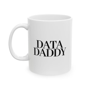 May include: White ceramic mug with a curved handle. The mug features the text "DATA DADDY" in black, stylized lettering. The mug is a standard size and shape, suitable for hot or cold drinks.