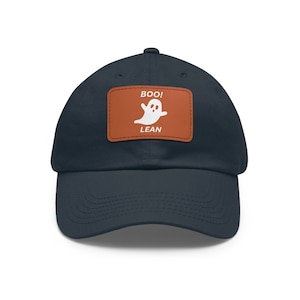 Op de afbeelding: Marineblauwe baseballcap met een bruine patch. De patch toont een witte spookafbeelding en de woorden "BOO!" en "LEAN". Een casual pet voor Halloween of dagelijks gebruik.