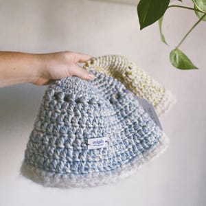 May include: Two crocheted hats, one blue and white and one yellow and white, with a white label that says "migdo" on the blue and white hat.