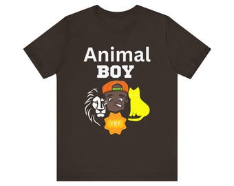 Op de afbeelding: Een bruin T-shirt met de tekst "Animal Boy" in witte letters. Het shirt heeft een cartoonillustratie van een jongen met een leeuw, een kat en een badge met de tekst "Yep".