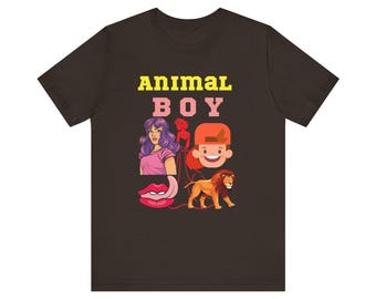 Op de afbeelding: Een bruin T-shirt met de tekst "Animal Boy" in gele en roze letters. Het shirt heeft een cartoonillustratie van een jongen met een rode pet, een leeuw, een vrouw met paars haar en een roze tong.